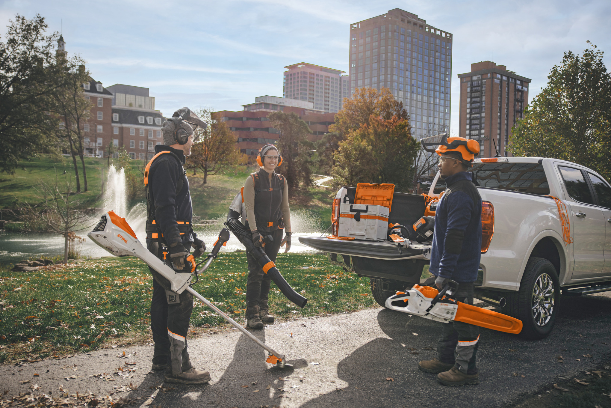 Een groep professionele tuinarchitecten staat rond hun voertuigen en maakt zich klaar om aan de slag te gaan met accumachines van STIHL. 