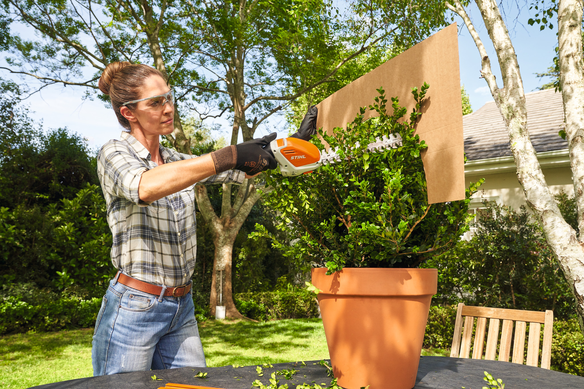 Een vrouw snoeit de buxus met de STIHL HSA 26 accugras- en buxusschaar met behulp van een kartonnen sjabloon in de vorm van een bol