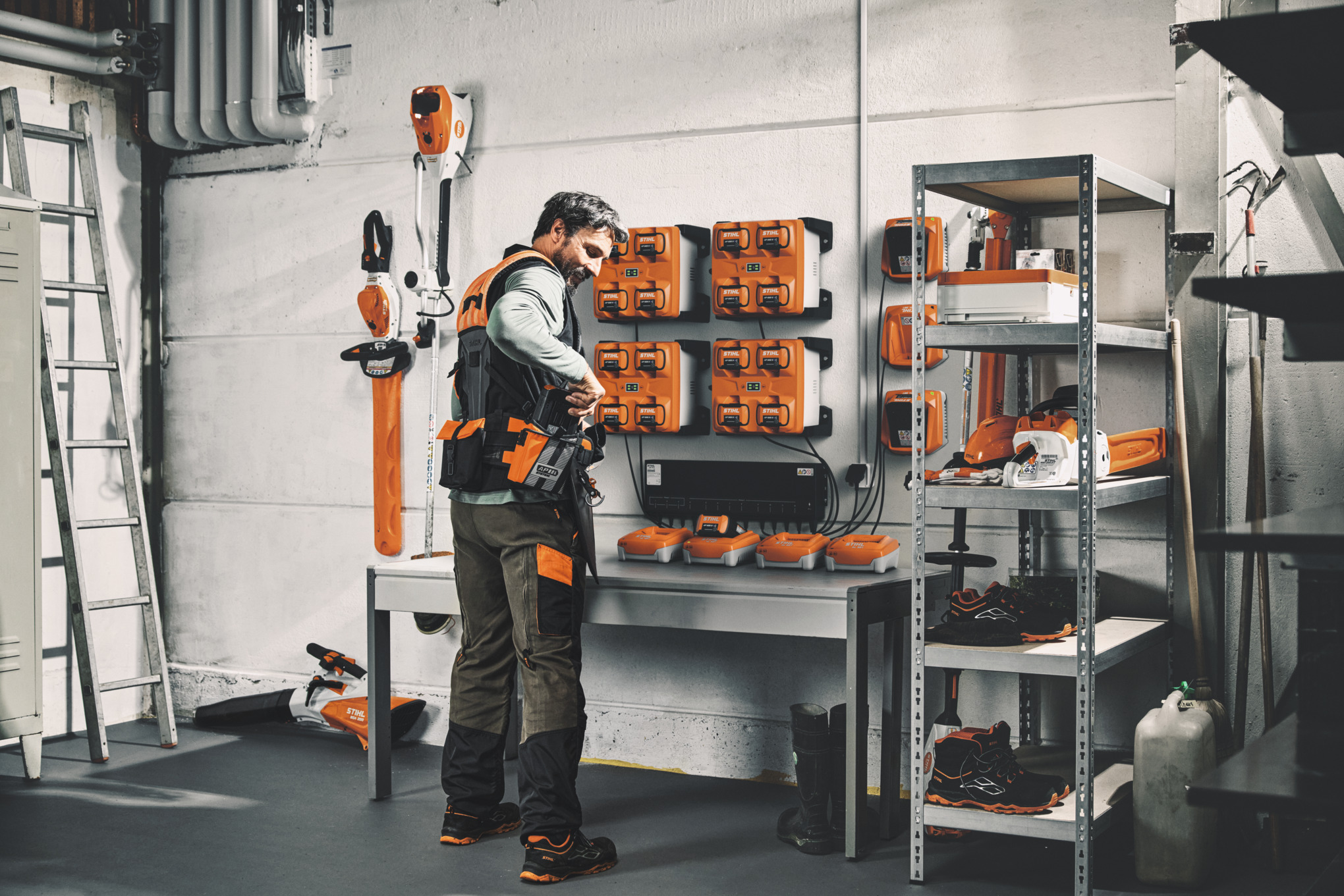 Man in een werkplaats maakt zijn ADVANCE X-Flex modulaire gordelsysteem klaar met opgeladen accu's van de CM 12 laadregelaar.