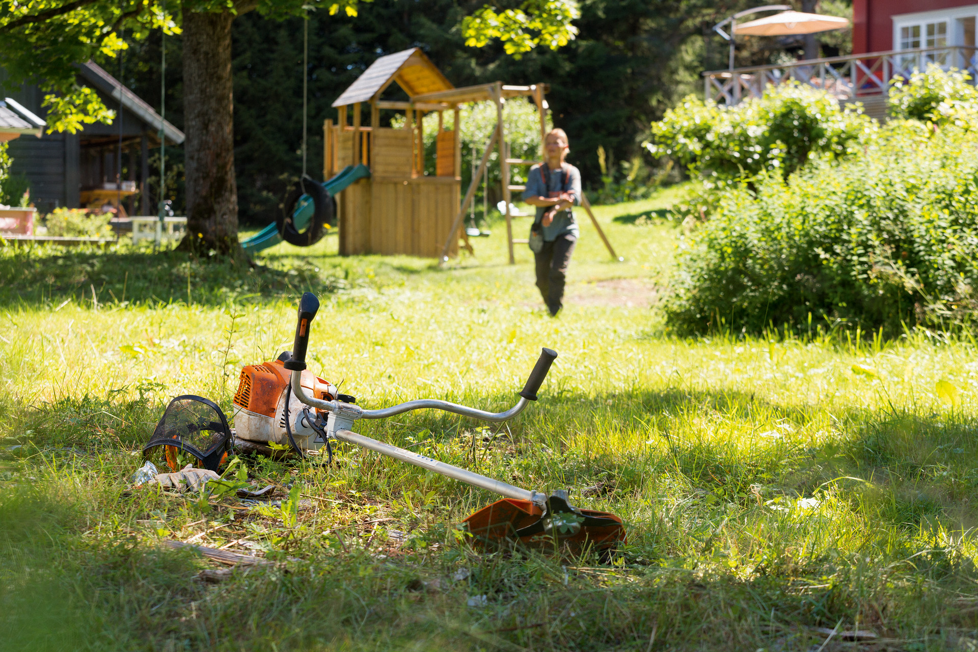 STIHL FS 240 bosmaaier ligt in het gras, op de achtergrond bereidt een man zich voor op het onderhoud