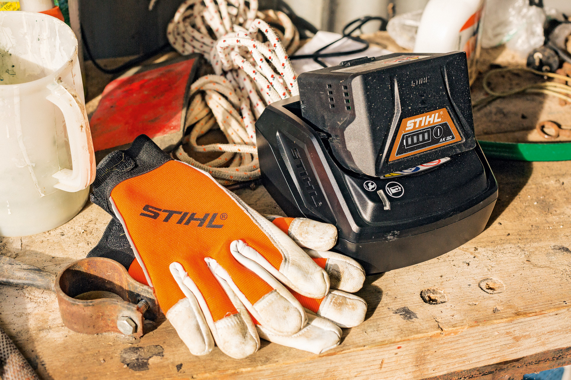 Opladen van lithium-ion-accu's uit de serie AK naast handschoenen en werkgereedschap van STIHL