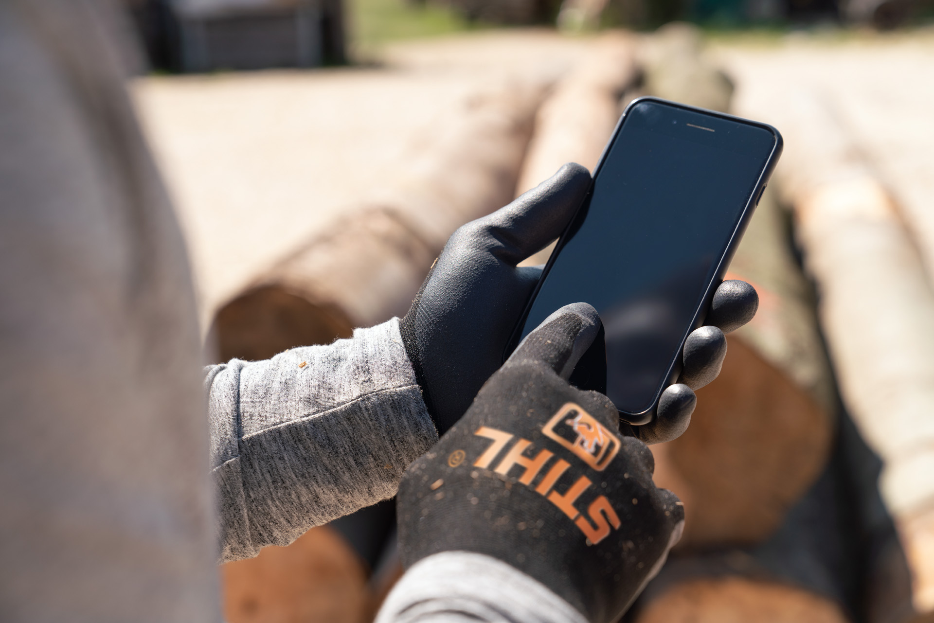 Een man met beschermende handschoenen van STIHL tikt op zijn smartphone.