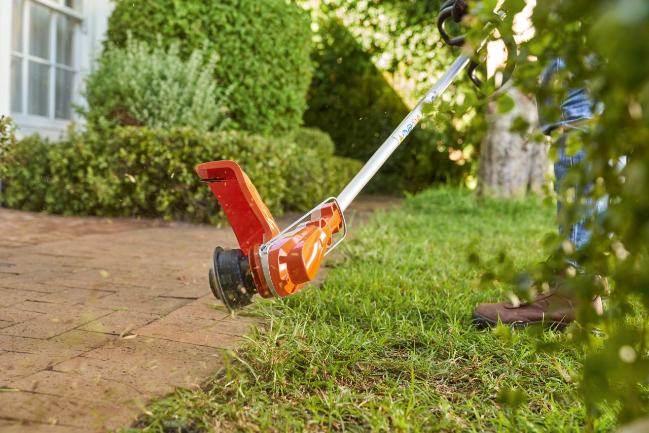 Persoon trimt graskanten met een accu grastrimmer
