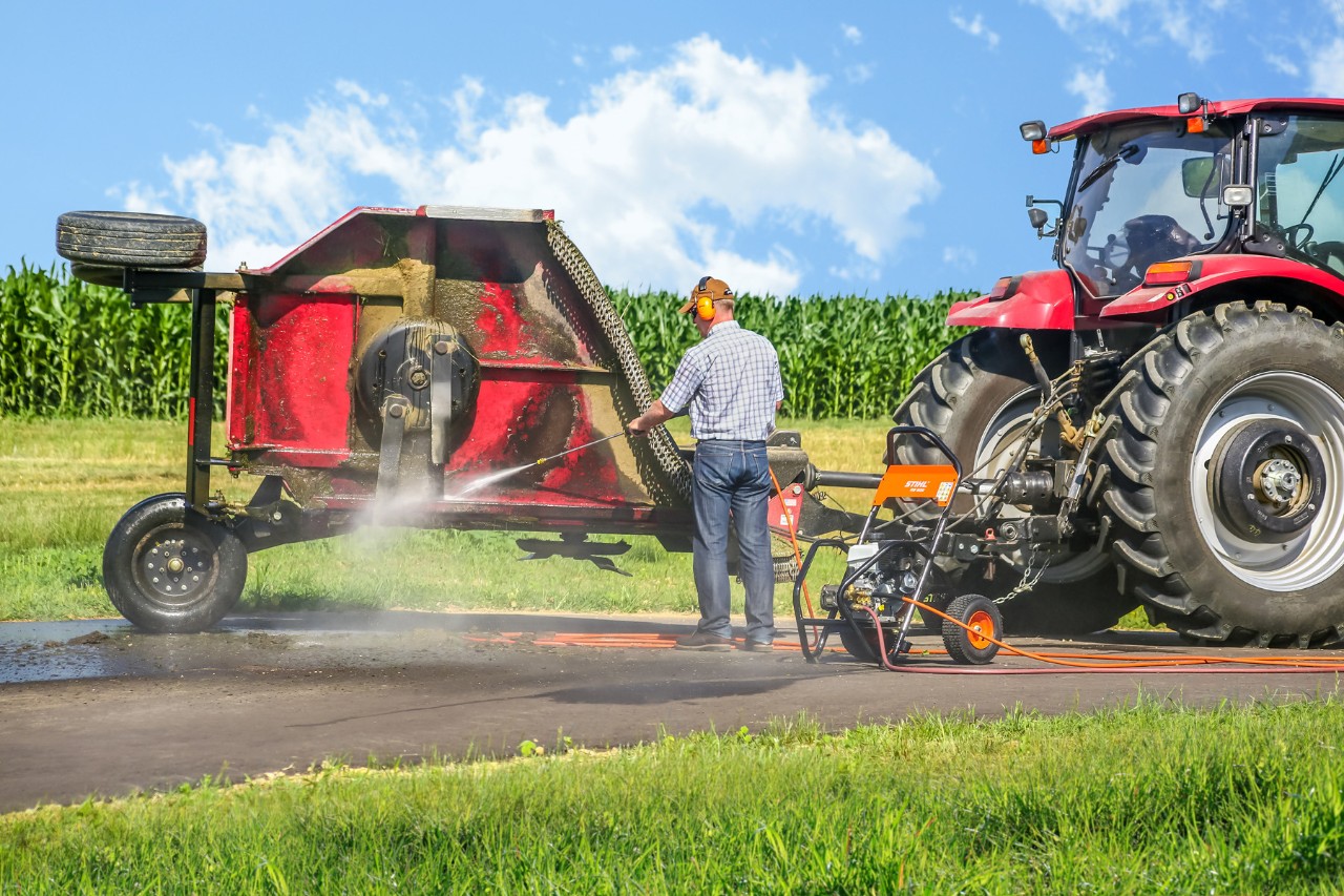 Man reinigt een tractor met aanhangwagen met een benzinehogedrukreiniger