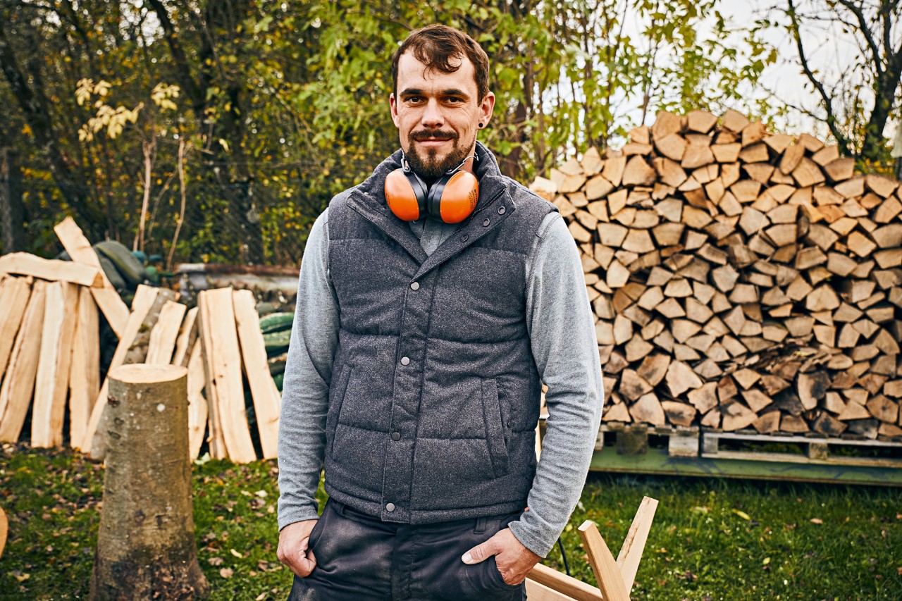 Mann mit STIHL Gehörschutz im Garten vor gestapelten Holzscheiten
