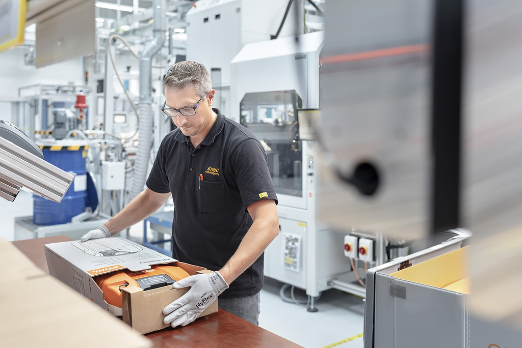 Een man met werkhandschoenen schuift een professionele accu voorzichtig in een doos