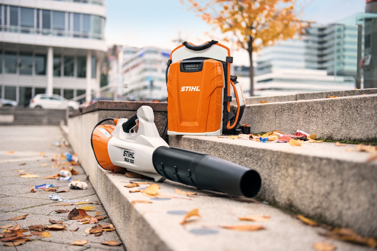 Op een stenen trap met enkele bladeren liggen de accubladblazer STIHL BGA 100 en de op de rug gedragen professionele accu STIHL AR 3000 L