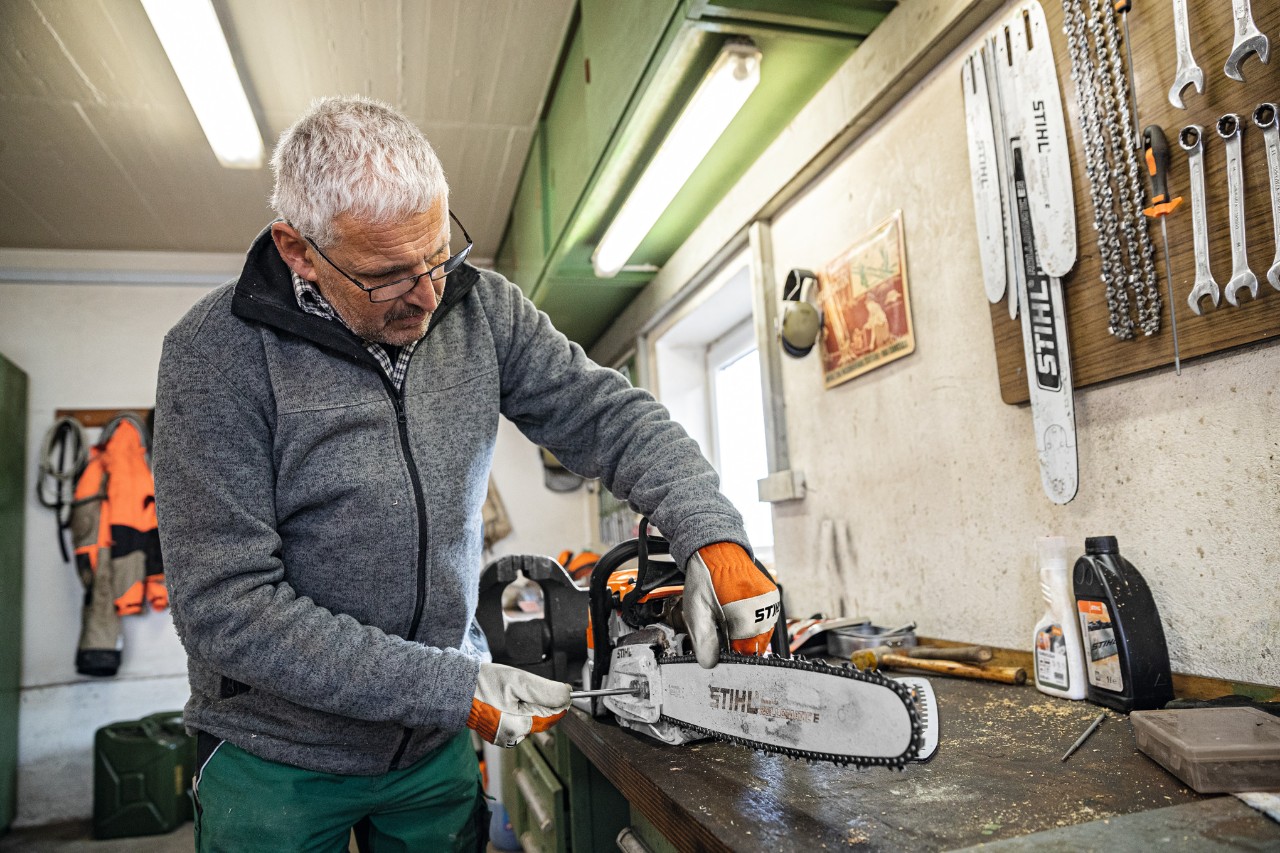 Een man in een werkplaats schroeft aan een kettingzaag met het zaagblad STIHL Rollomatic E 