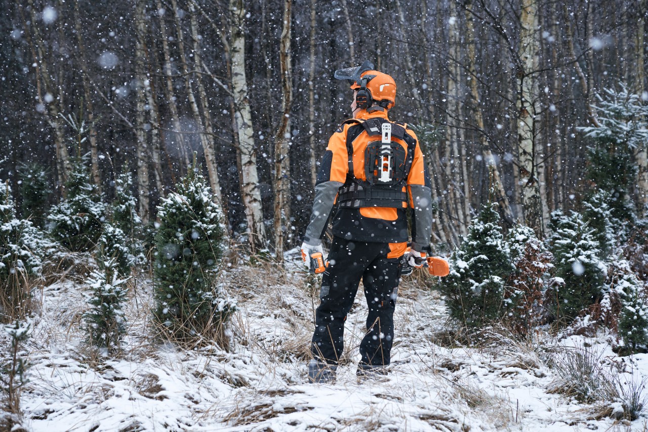 Rug van een bosarbeider in een besneeuwd bos, met STIHL veiligheidsuitrusting met modulair gordelsysteem en accumachines voor het onderhoud van jonge bosbestanden