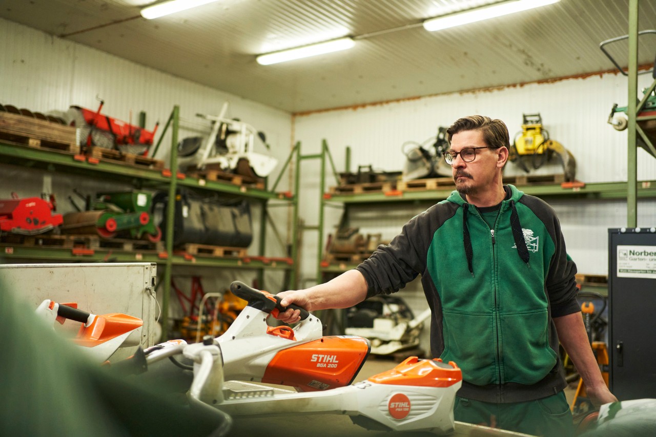 Een man in een werkplaats staat achter een werkoppervlak met STIHL accumachines en neemt de STIHL BGA 200 accubladblazer