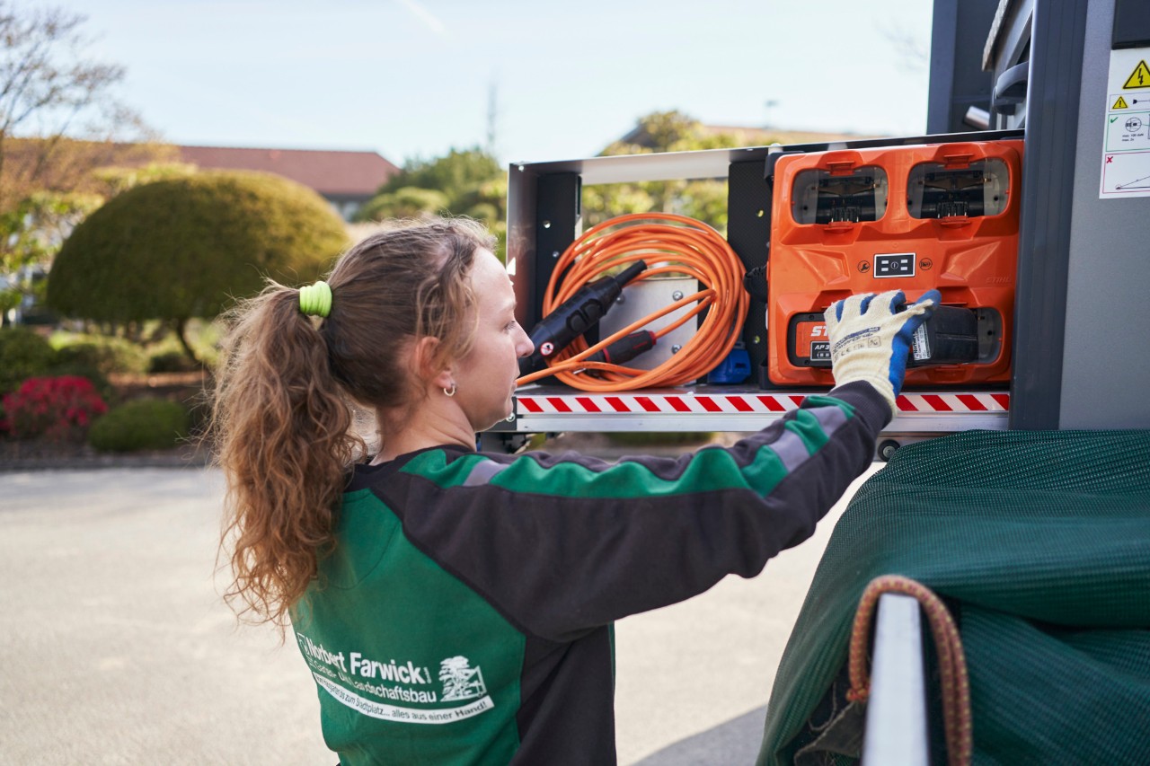 Een medewerkster van Farwick GmbH laadt een bottTainer op een werkvoertuig met accu's