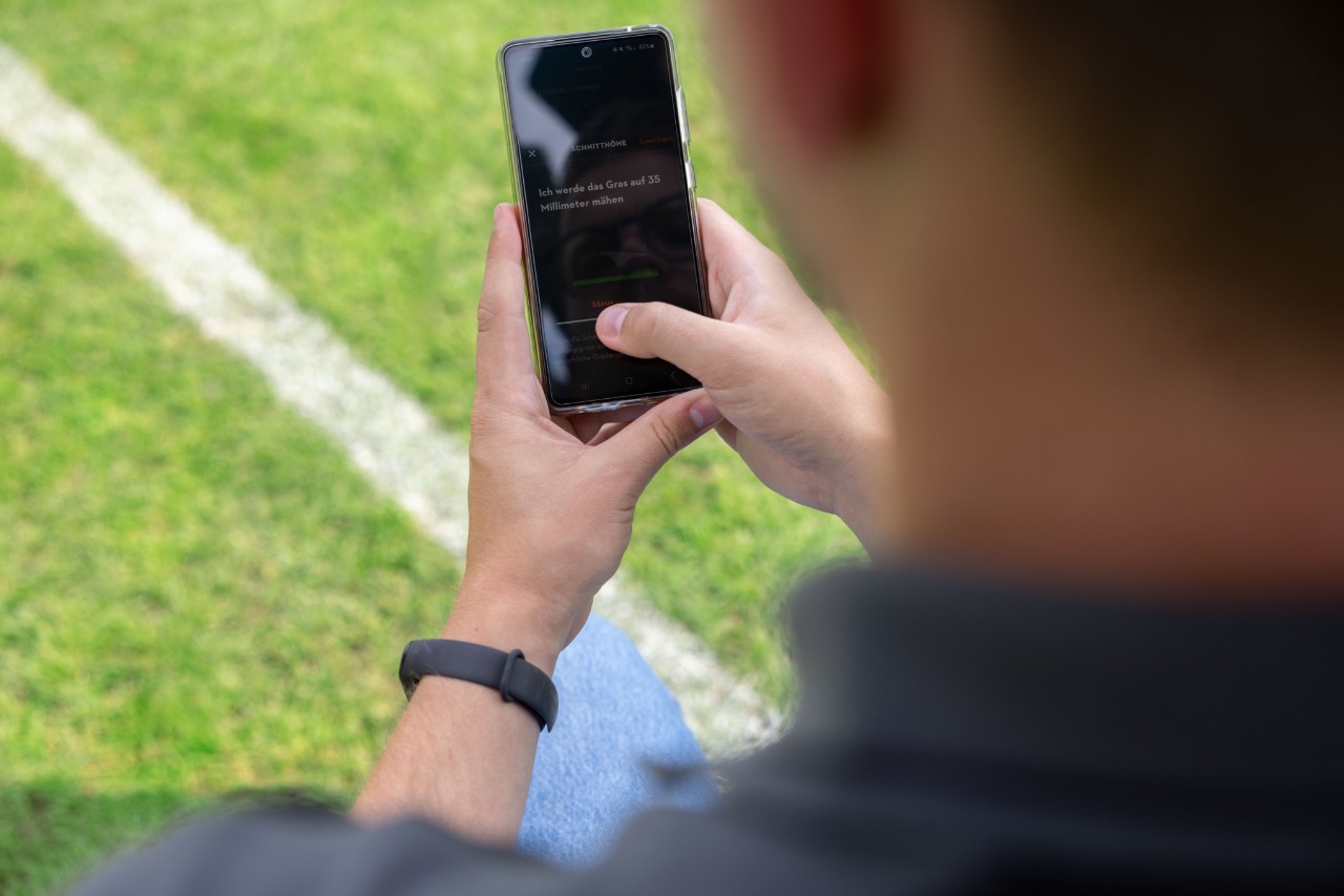 Een persoon op een sportveld heeft de MY iMOW® app op een mobiele telefoon geopend