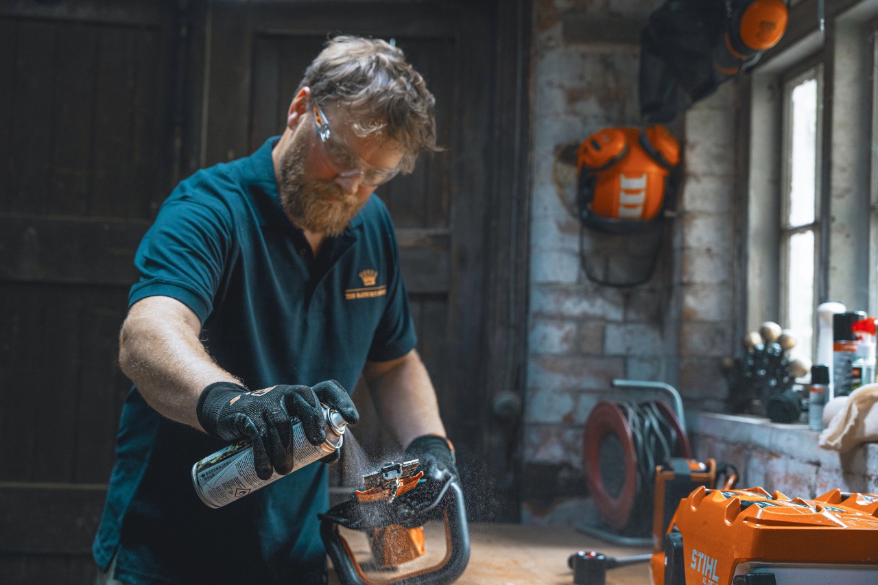 Een man in een werkplaats spuit een heggenschaar in met STIHL Superclean