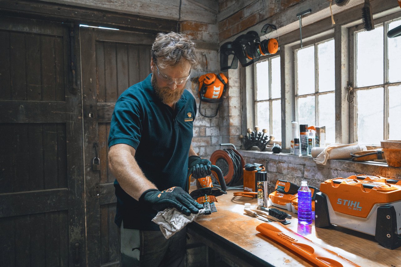 Een man in een werkplaats veegt een STIHL heggenschaar af met een doek