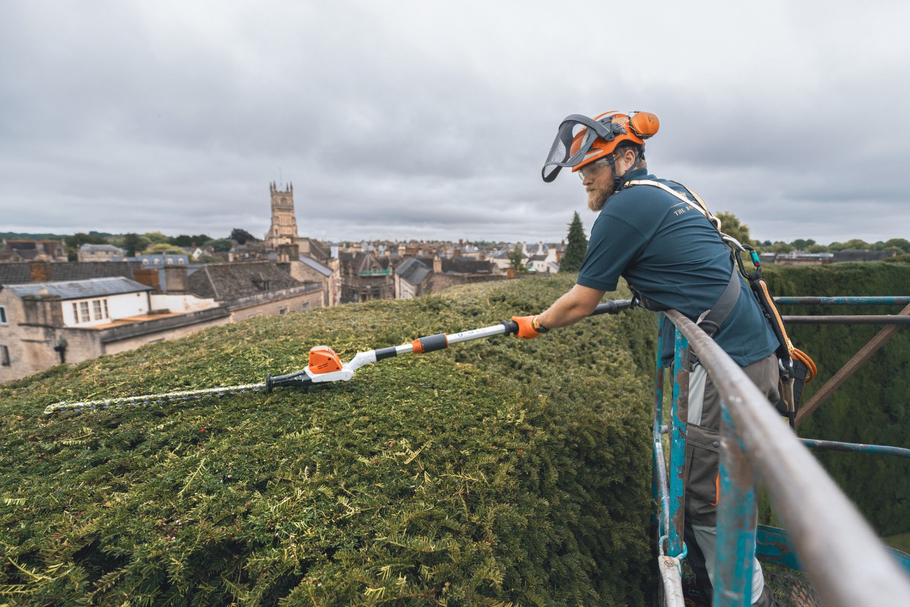 Een professional snoeit op een hoogwerker de bovenkant van de heg van het Bathurst Estate met een STIHL accuheggenschaar