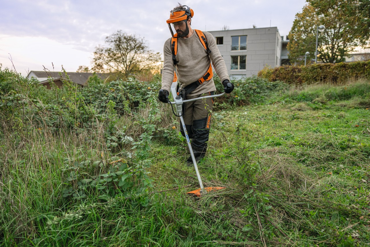 Een man in STIHL veiligheidsuitrusting maait een wild overwoekerd stuk grond met een STIHL FSA 200 accubosmaaier