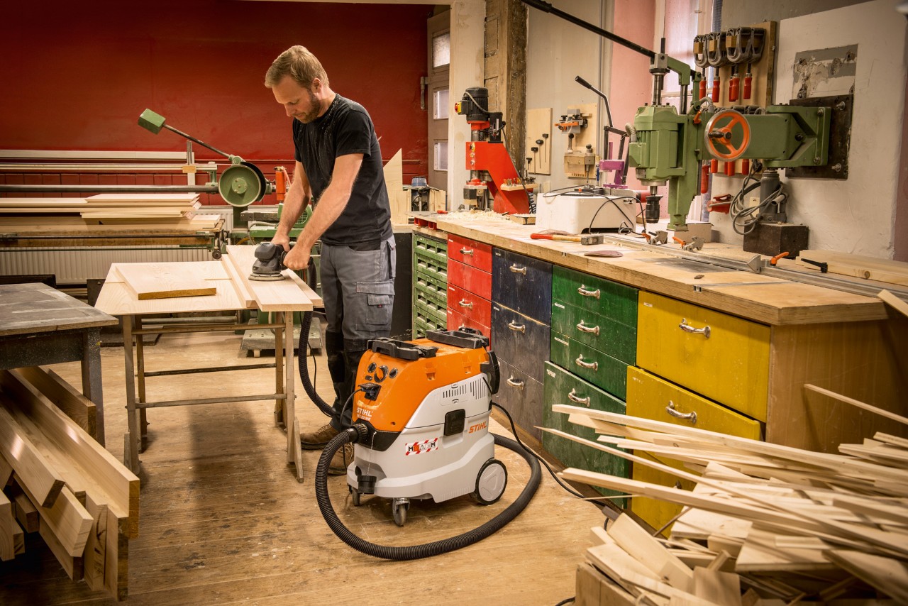 Man gebruikt een STIHL SE 133 ME alleszuiger in een werkplaats terwijl hij met houten planken werkt