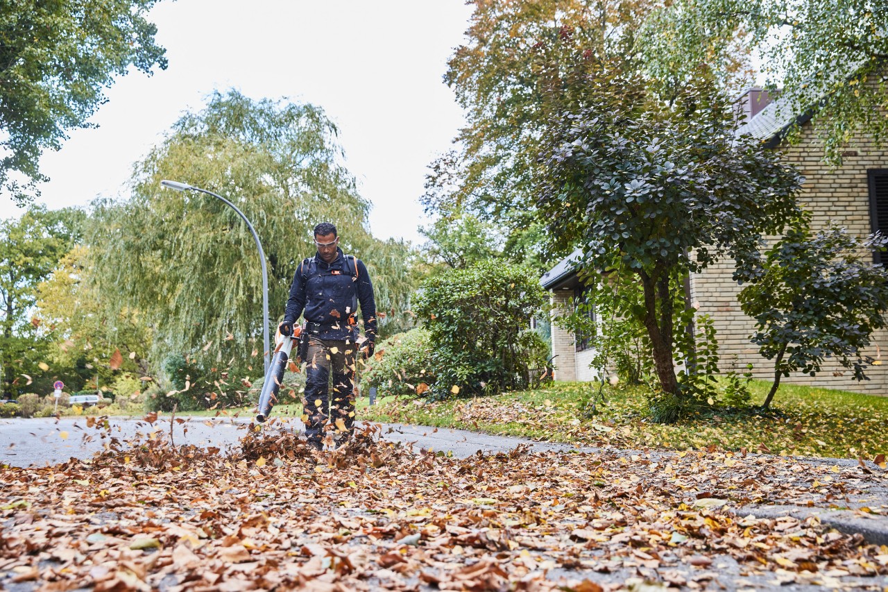 Een hovenier verwijdert bladeren van de straat met de STIHL BGA 200 accubladblazer .