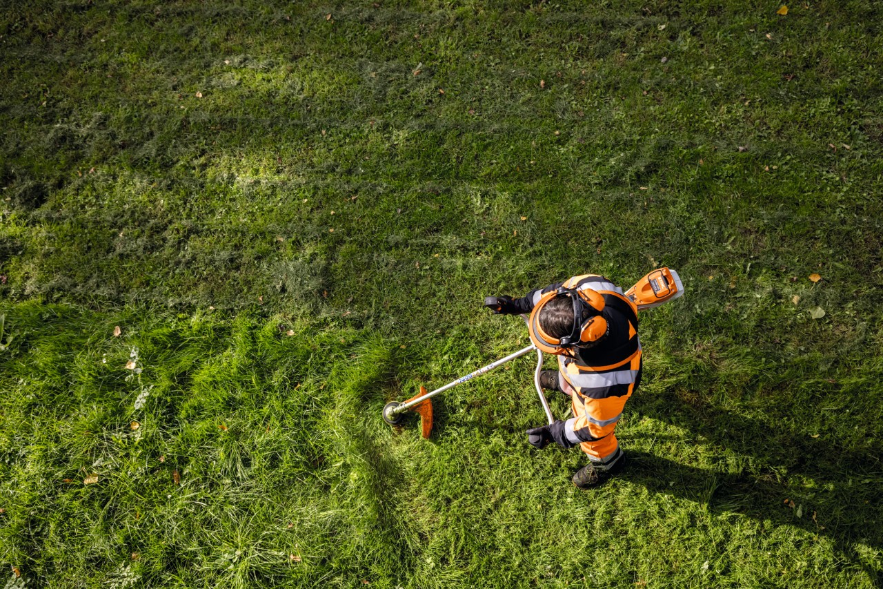 Hovenier in oranje werkkleding maait hoog gras met de STIHL FSA 135 accu-bosmaaier.