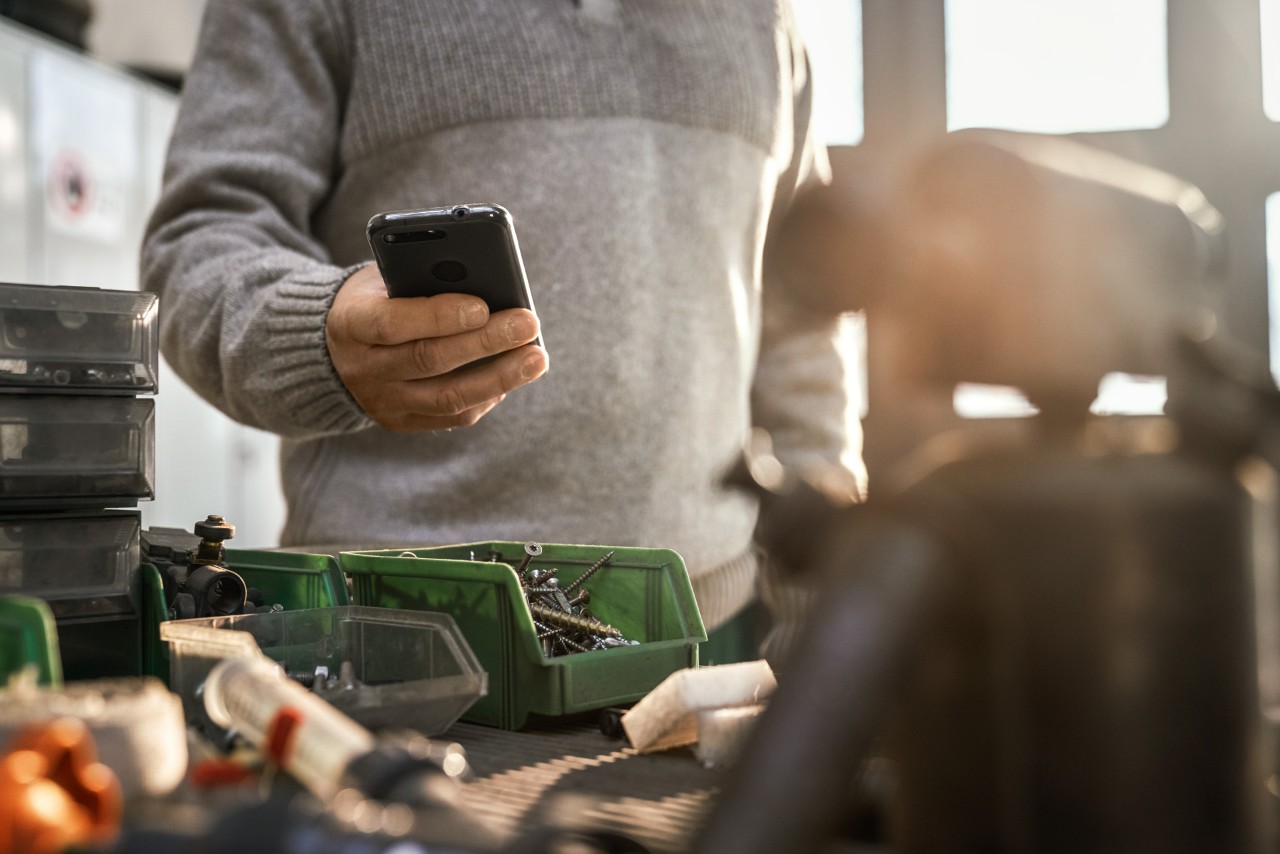 Persoon met smartphone in een werkplaats