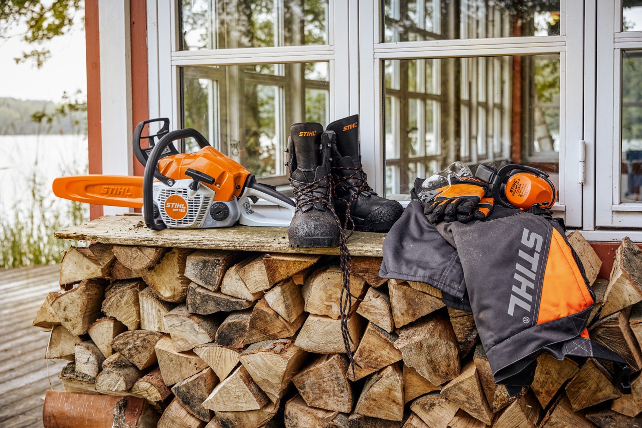 STIHL beschermende kleding en MS 162 liggen op een rek boven gestapeld brandhout
