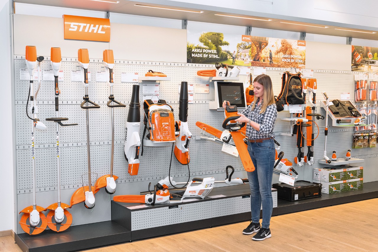 Een jonge vrouw voor een schap bij een STIHL dealer wil gratis met een STIHL kettingzaag uitproberen 