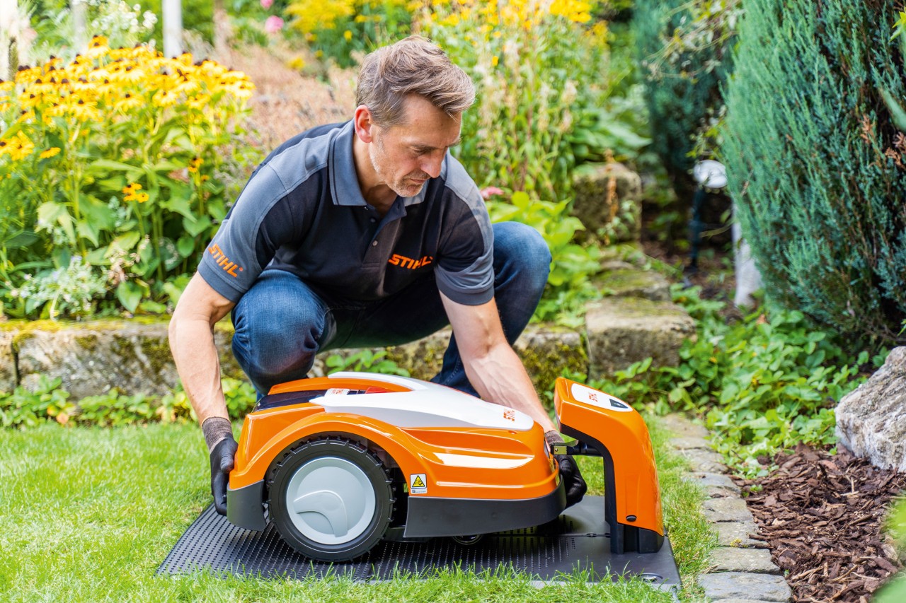 Een STIHL dealer plaatst een STIHL iMOW robotmaaier in het laadstation in een tuin