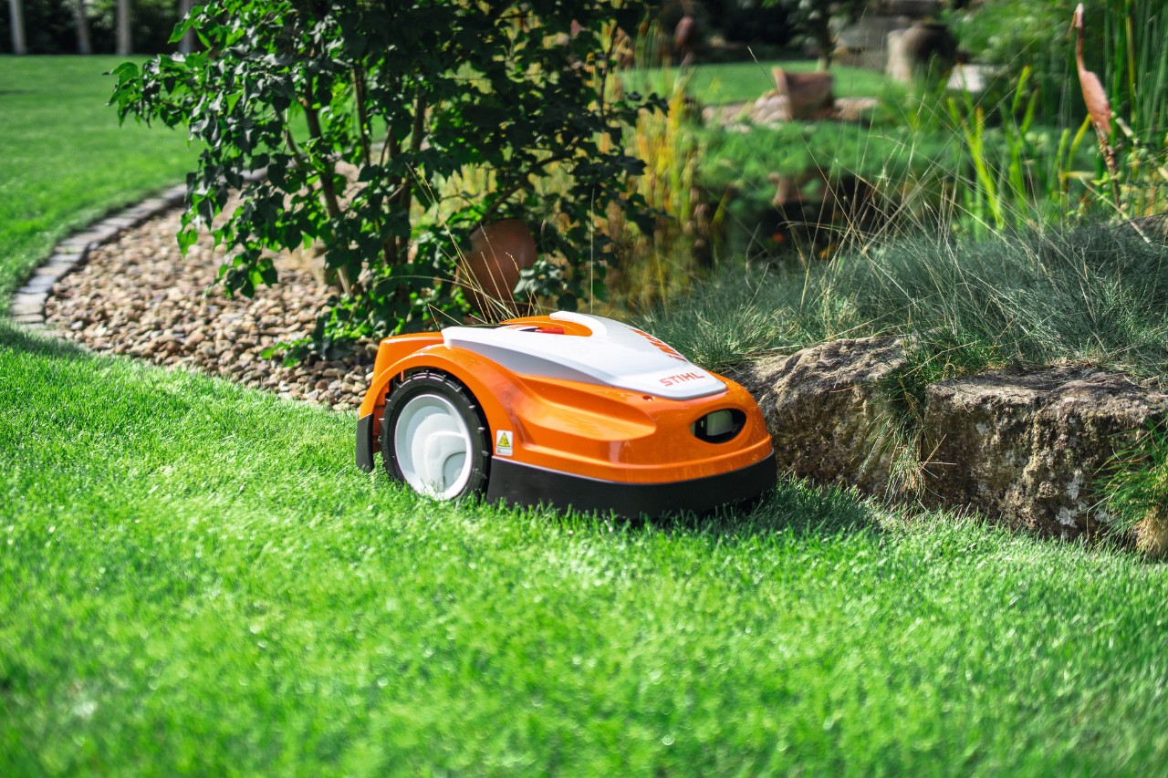 STIHL iMOW RMI 422 maait een stuk gras in de tuin langs de rand van een kleine stenen muur.