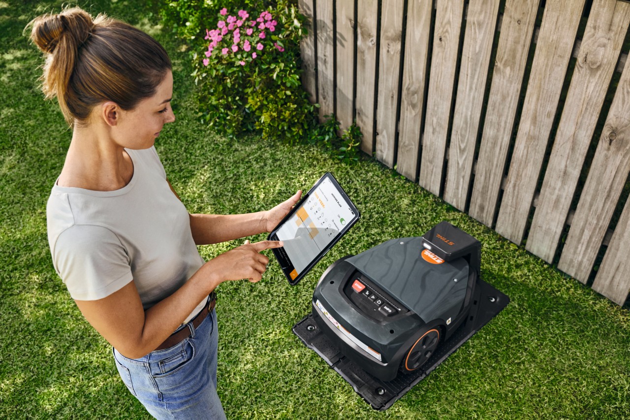 Vrouw bedient de STIHL iMOW® EVO via een tablet in haar tuin