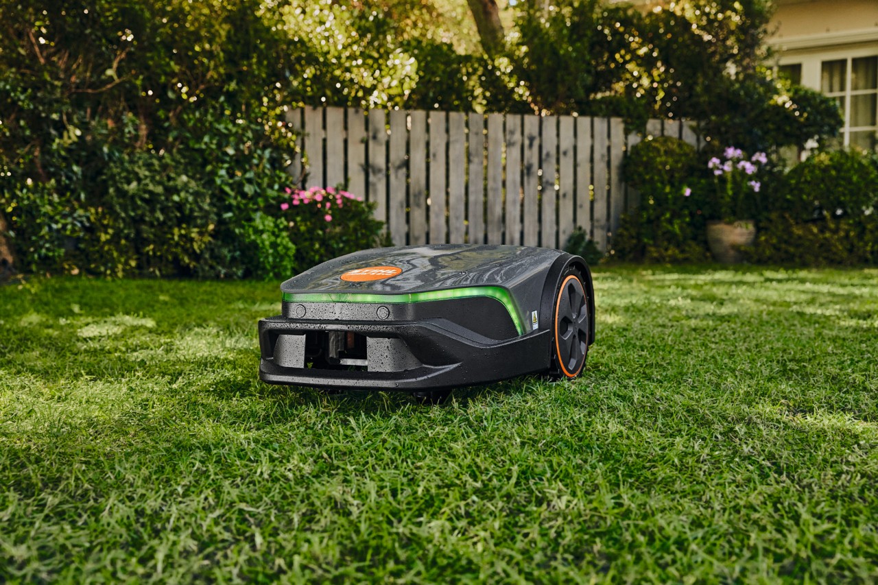 Een iMOW® EVO maait in de tuin voor een huis en een hangmat het goed onderhouden gazon.