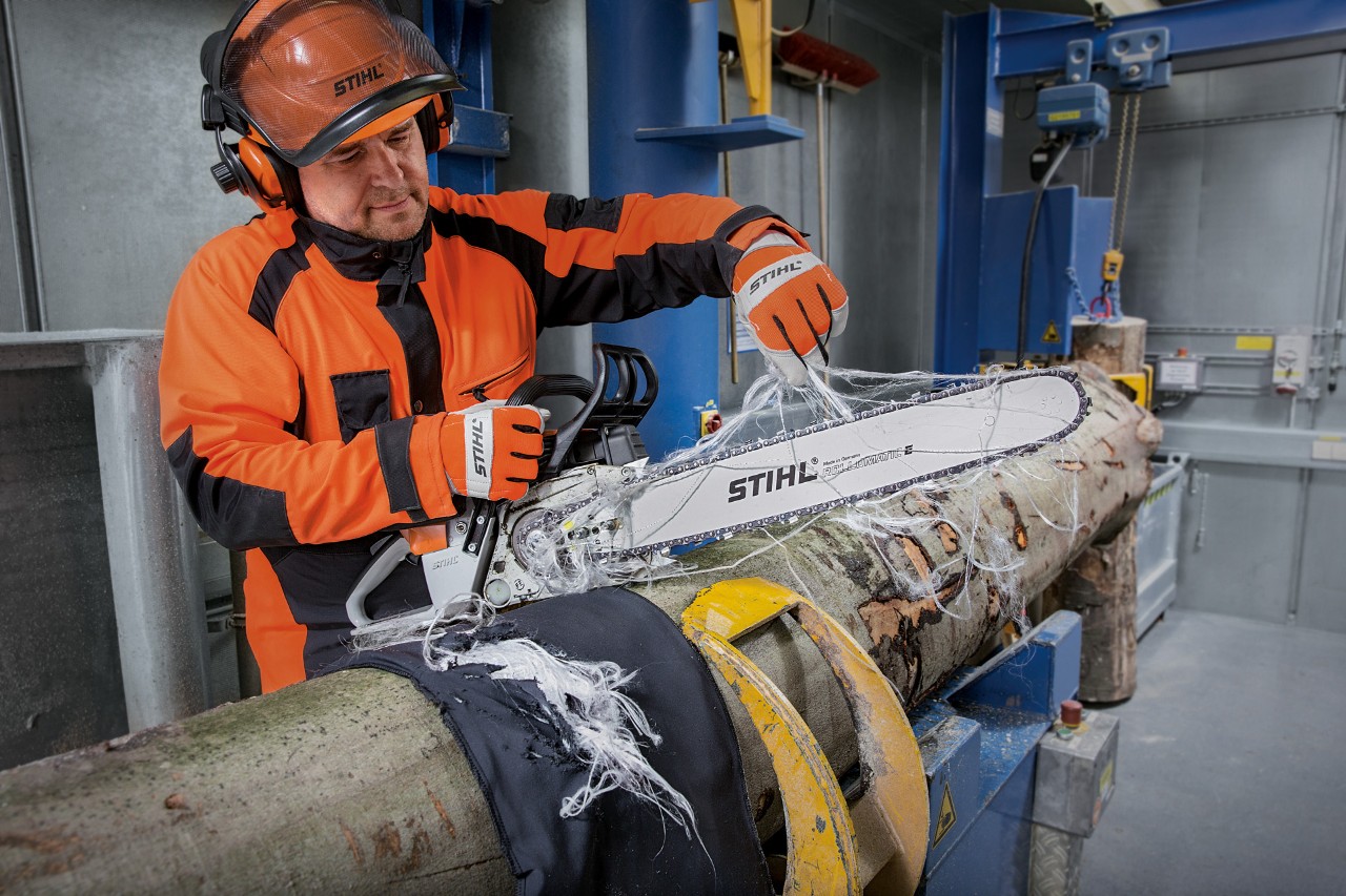 Persoon in beschermende kleding test de snijbestendigheid van de STIHL snijbestendige kleding met een STIHL kettingzaag