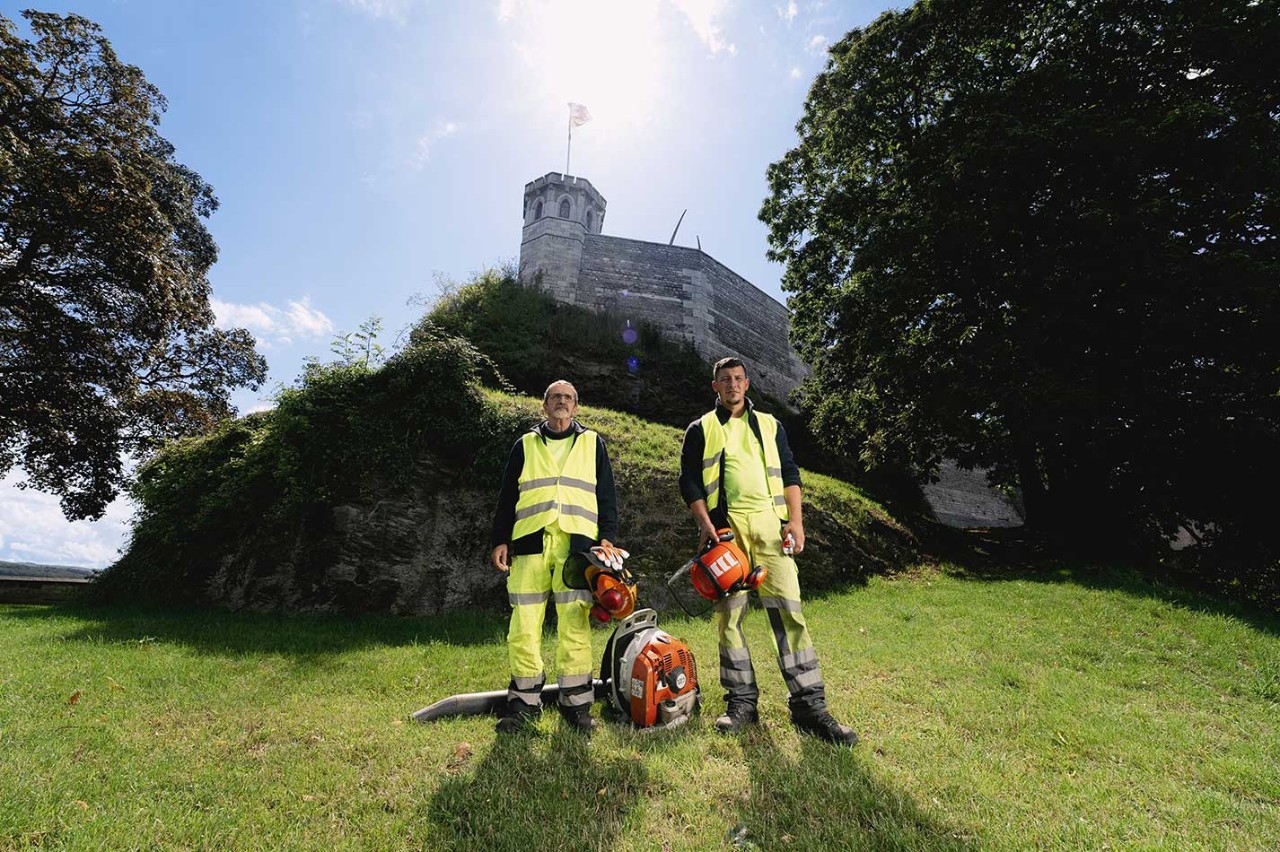 Bernard en Jérémy poseren met een blabdlazer en veiligheidskledij in het groen rond de Citadel van Namen