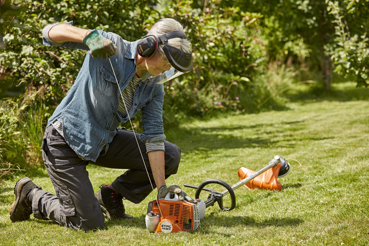 Vrouw met gehoor- en gezichtsbescherming staat op het punt om een STIHL benzinekantenmaaier FS 56 R te starten