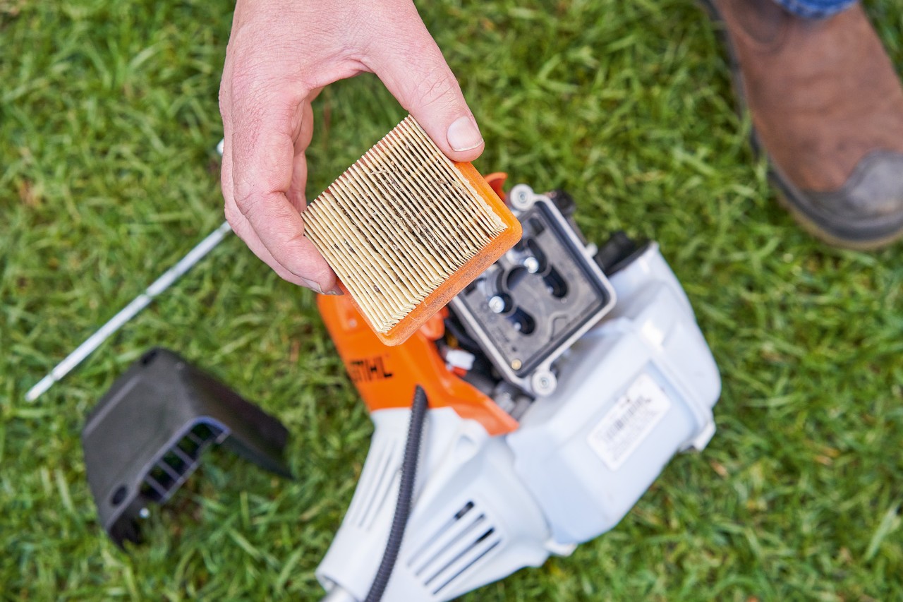 Iemand verwijdert het luchtfilter uit een STIHL bosmaaier om te reinigen 