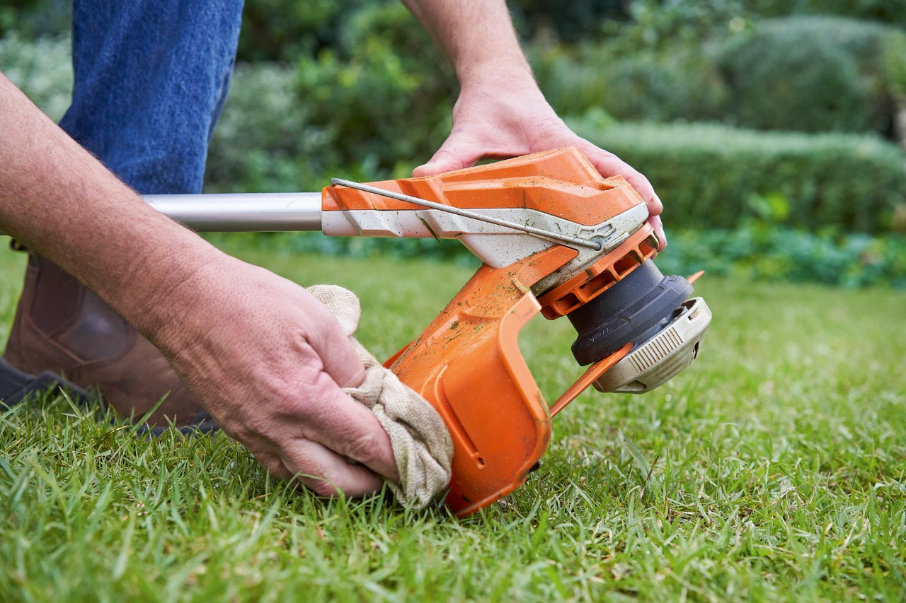 Iemand reinigt de beschermkap van een STIHL grasmaaier met een vochtige doek