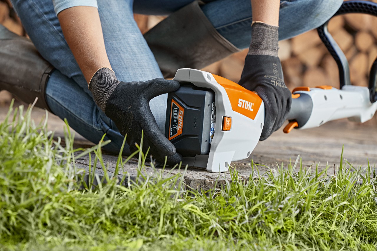 Iemand knielt op de grond en verwijdert een accu uit een STIHL FSA 57 accukantenmaaier