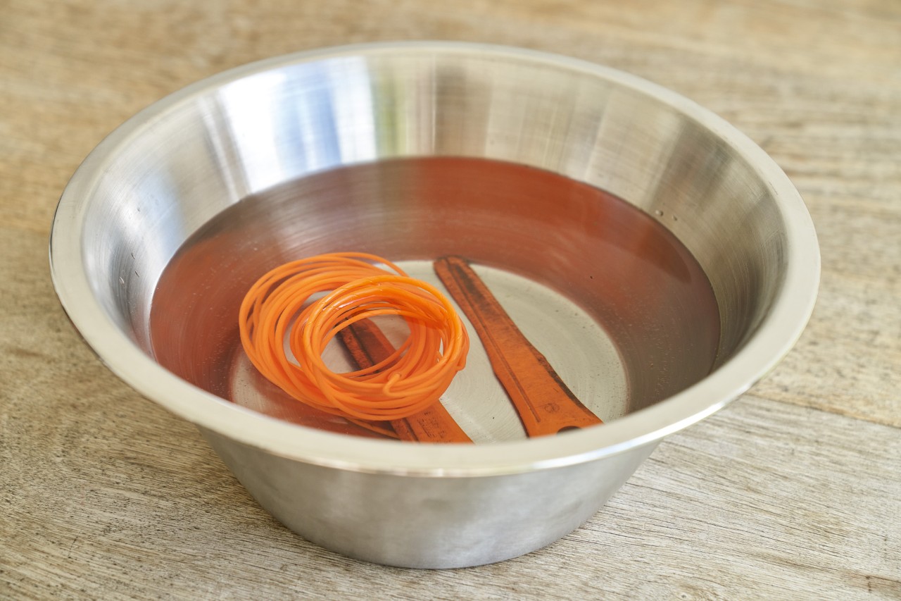 Maaidraad en PolyCut-mes van een bosmaaier liggen in een metalen kom met water op hout