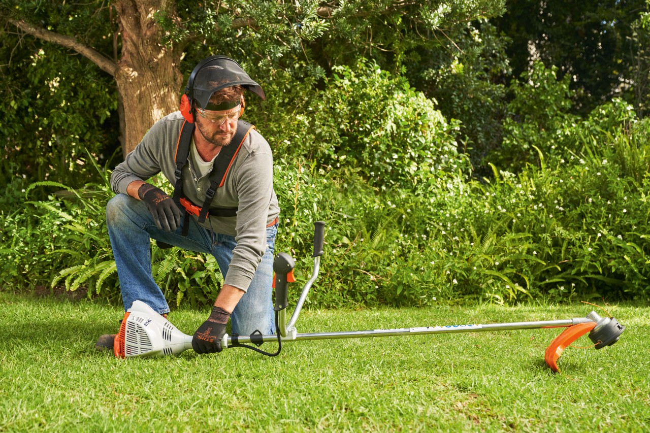 Man legt de STIHL FS 56 benzinekantenmaaier op de grond om deze te starten