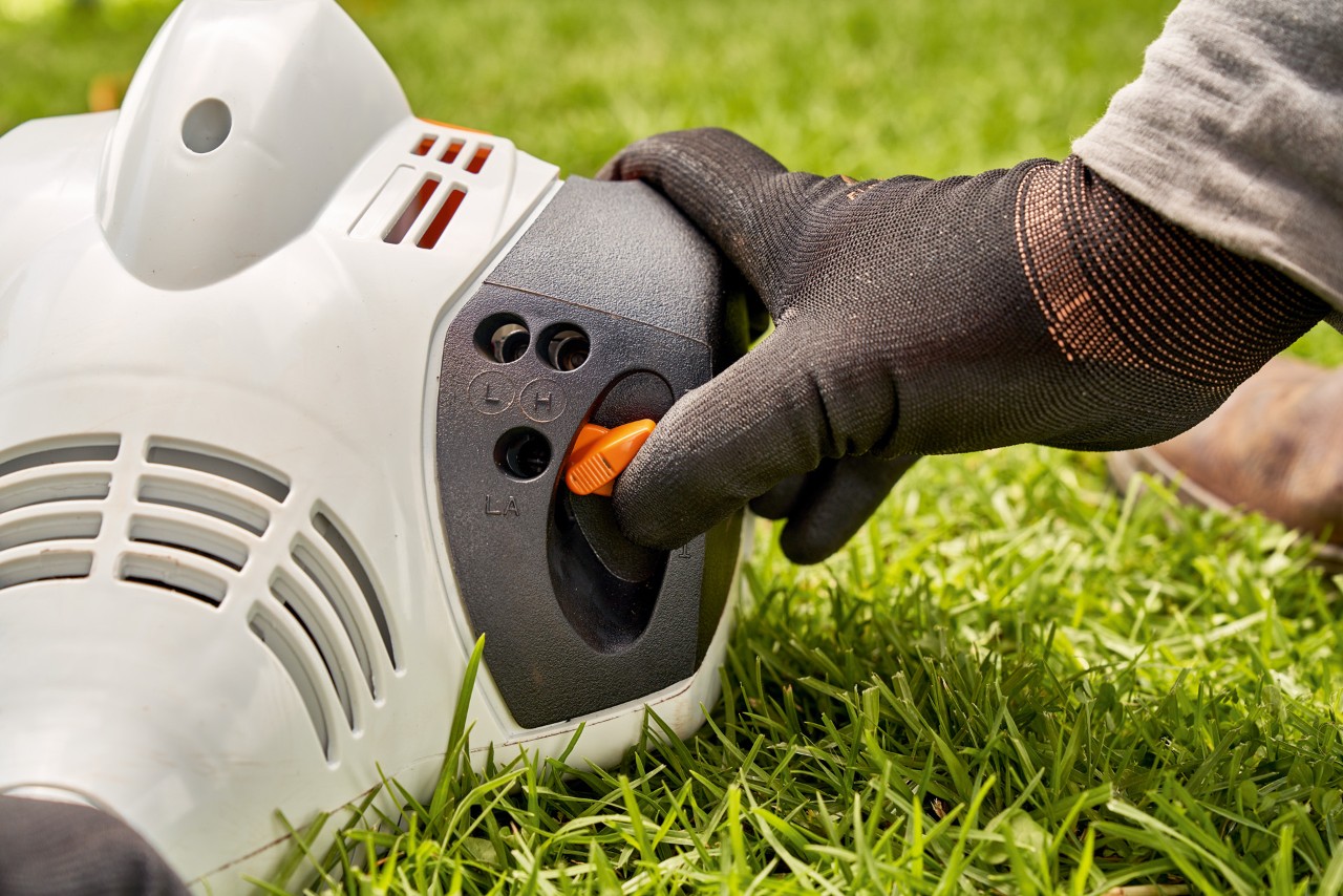 Man drukt de hendel van de STIHL FS 56 benzinekantenmaaier in om deze te starten