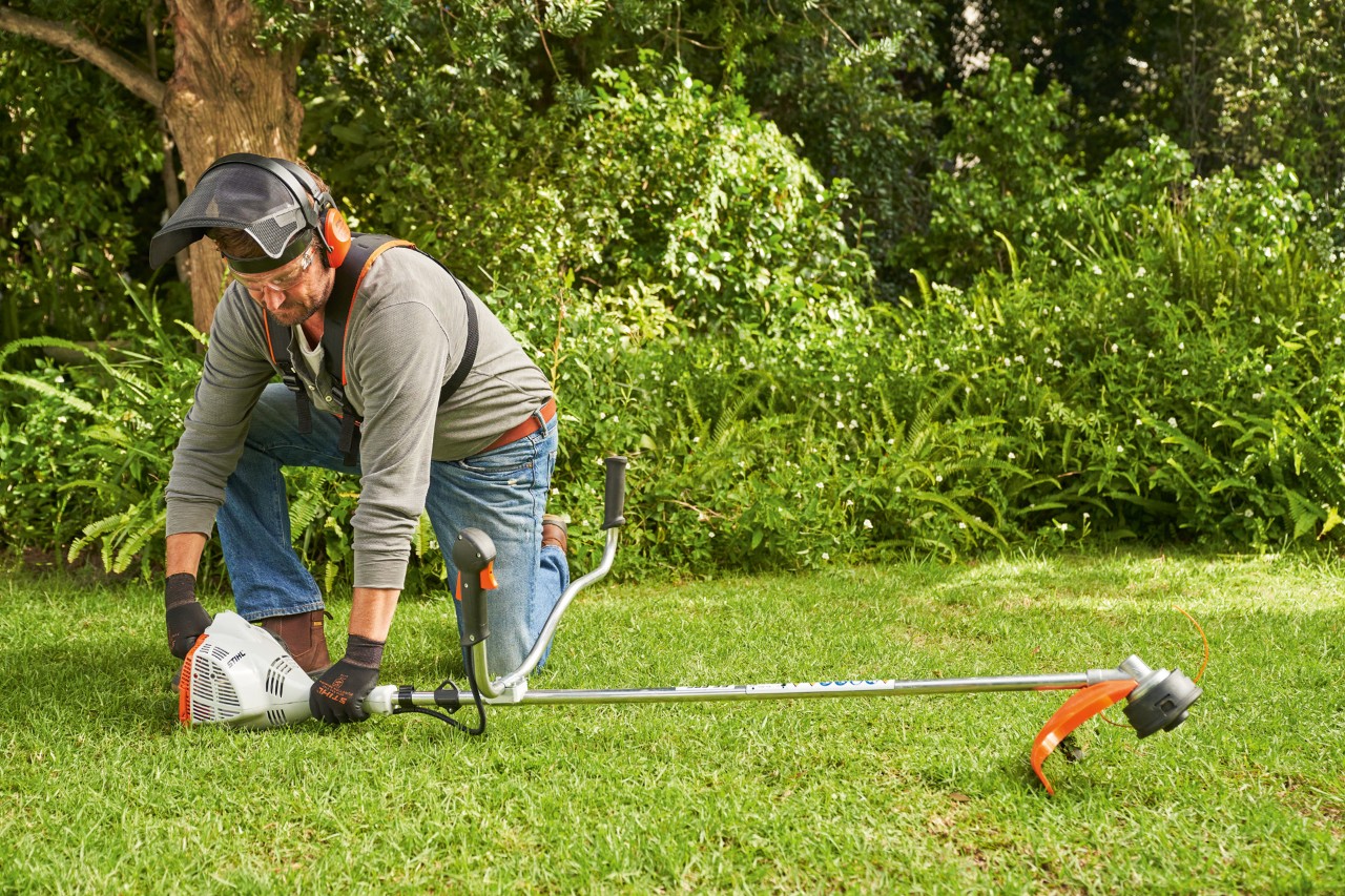 Man drukt de STIHL FS 56 benzinekantenmaaier stevig op de grond om deze te starten