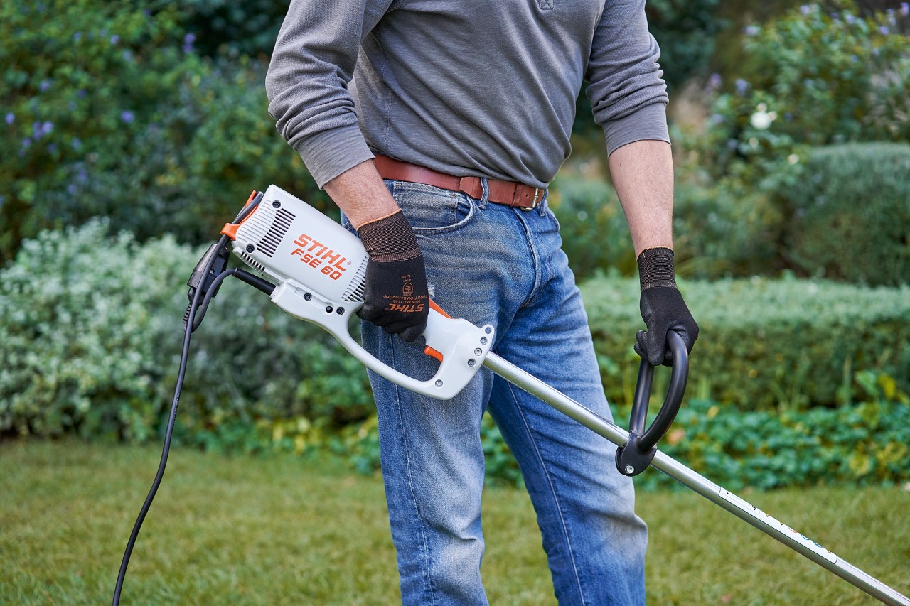 Man met veiligheidshandschoenen neemt de STIHL FSE 60 elektrische kantenmaaier met beide handen vast