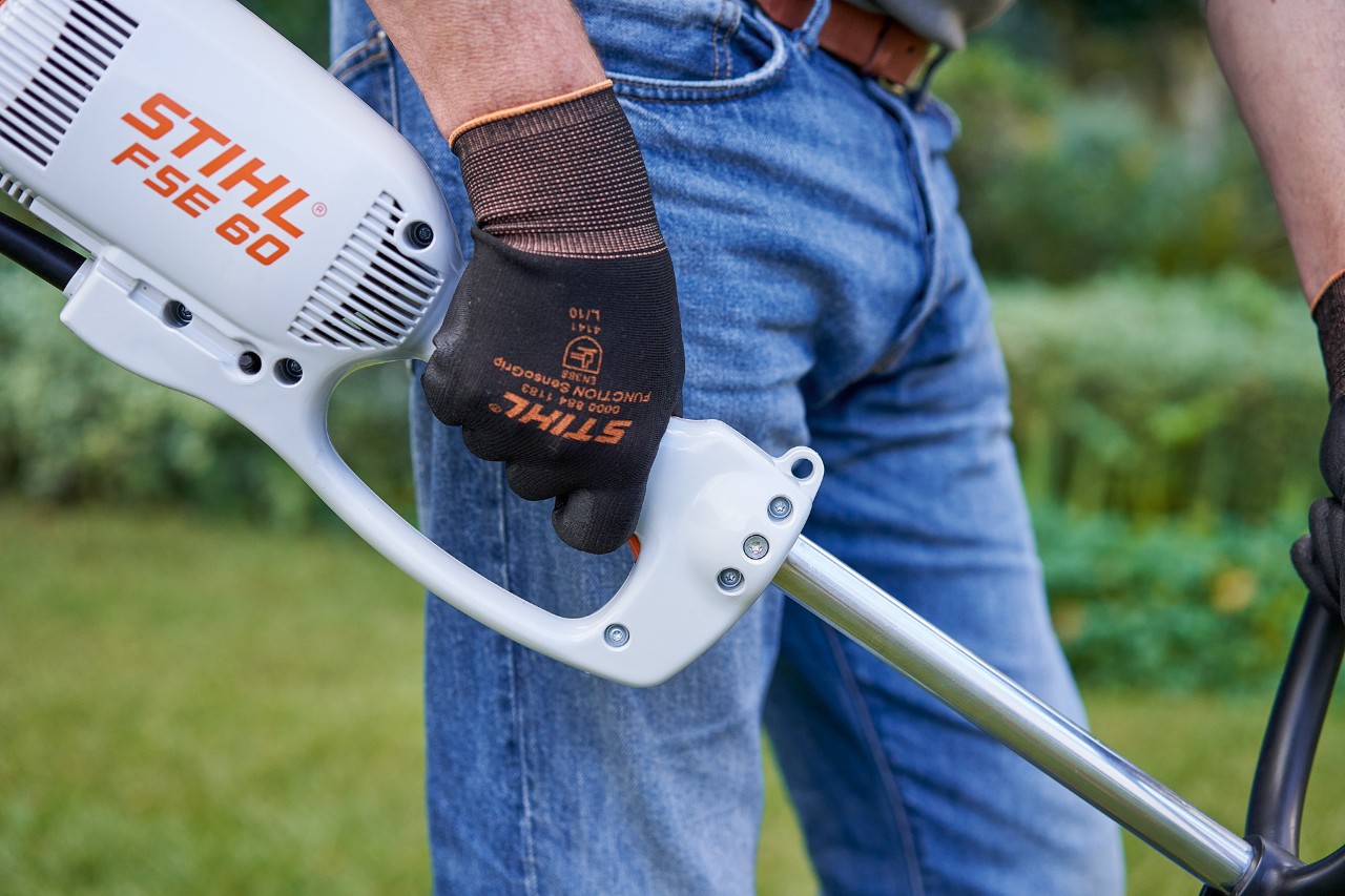 Man drukt op de schakelaar op de bedieningshendel van de STIHL FSE 60 elektrische kantenmaaier