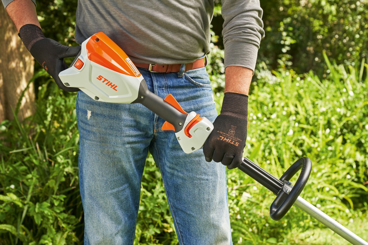 Man met veiligheidshandschoenen controleert de accu van de STIHL FSA 60 accukantenmaaier om de bosmaaier te starten