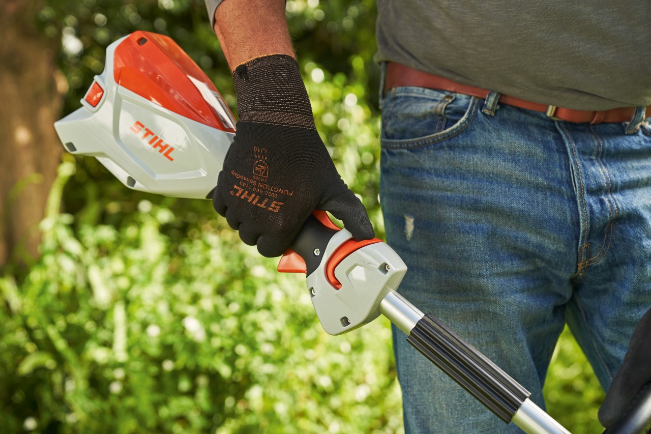 Man met veiligheidshandschoenen schuift de ontgrendelingsschuif van de STIHL FSA 60 accukantenmaaier naar de beugelgreep
