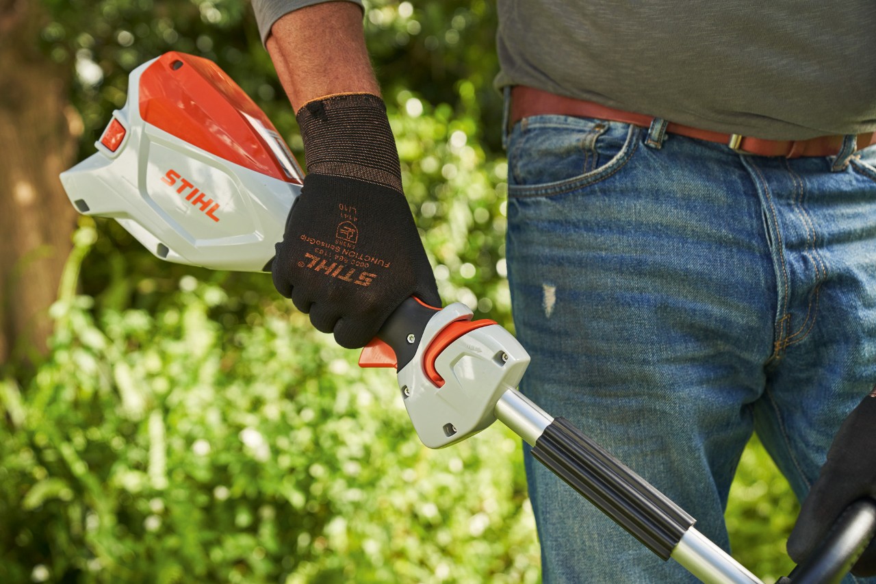 Man met veiligheidshandschoenen drukt de gashendelvergrendeling van de STIHL FSA 60 accukantenmaaier in 
