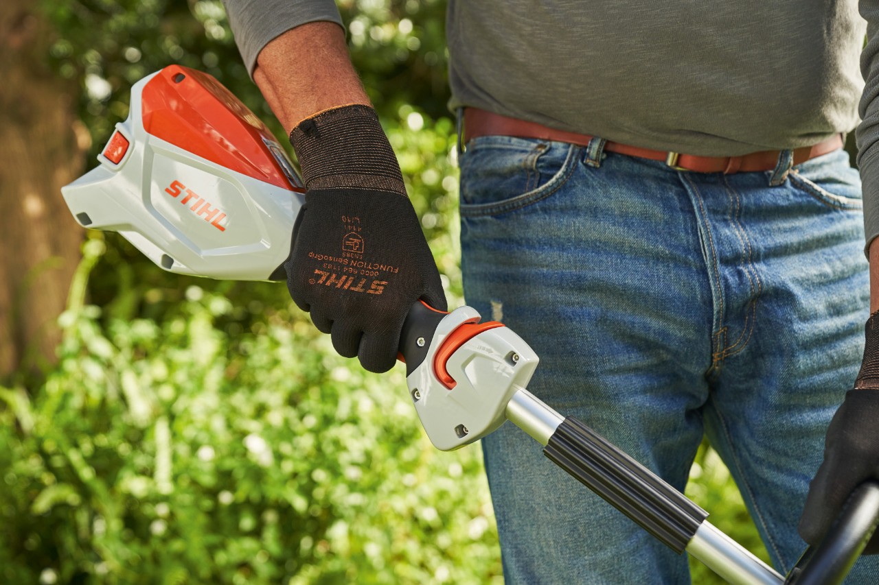 Man met veiligheidshandschoenen bedient de bedieningshandgreep van de STIHL FSA 60 accukantenmaaier om deze te starten