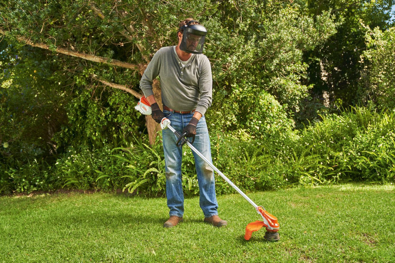 Een man met gezichtsbescherming maait het gazon in een tuin met de STIHL FSA 60 accukantenmaaier