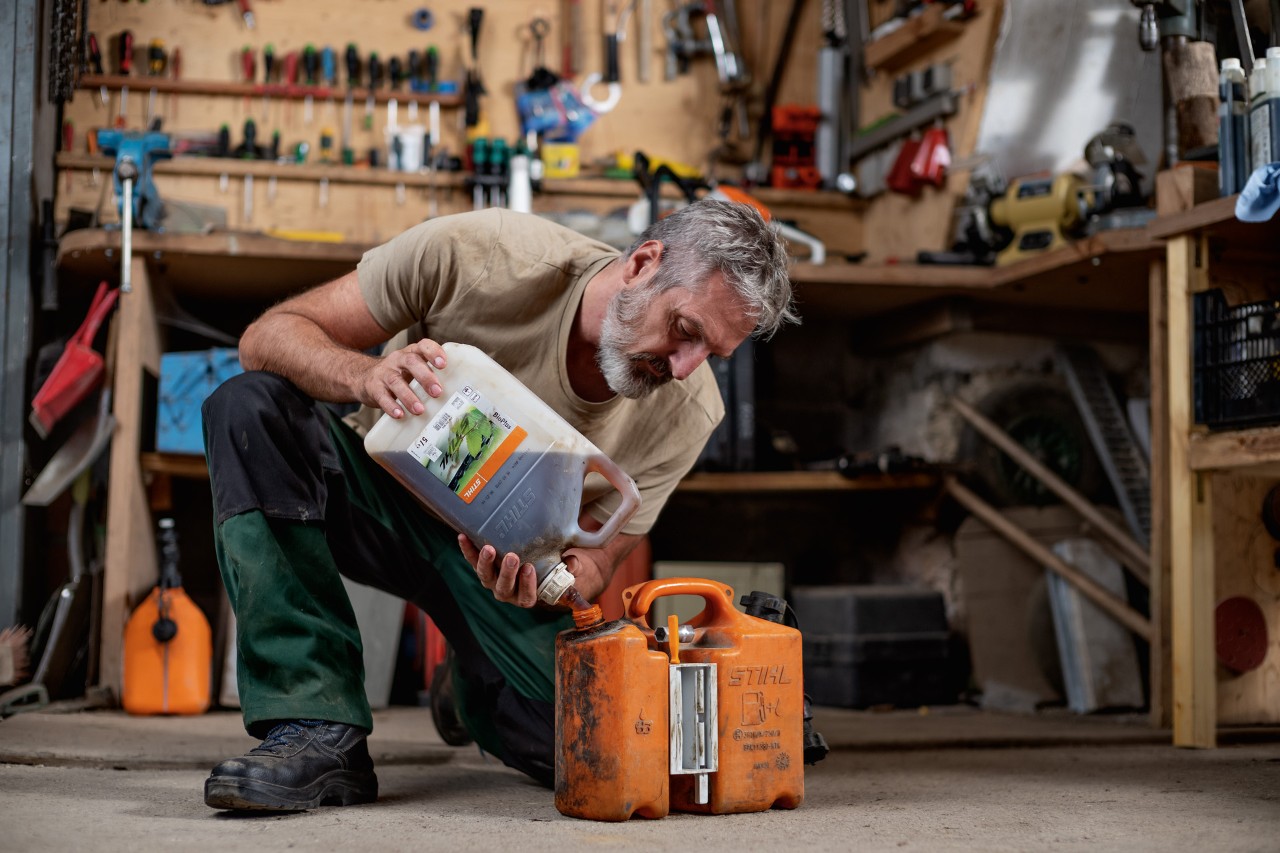 Een combinatiebus op een werkbank tussen bussen STIHL MotoMix en BioPlus kettingolie, met een STIHL MS 261C benzinekettingzaag op de achtergrond.