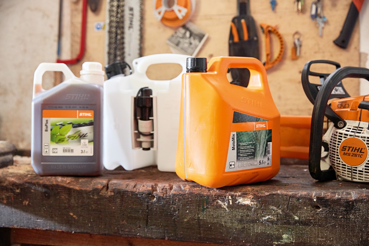 Een combinatiebus op een werkbank tussen bussen STIHL MotoMix en BioPlus kettingolie, met een STIHL MS 261C benzinekettingzaag op de achtergrond.