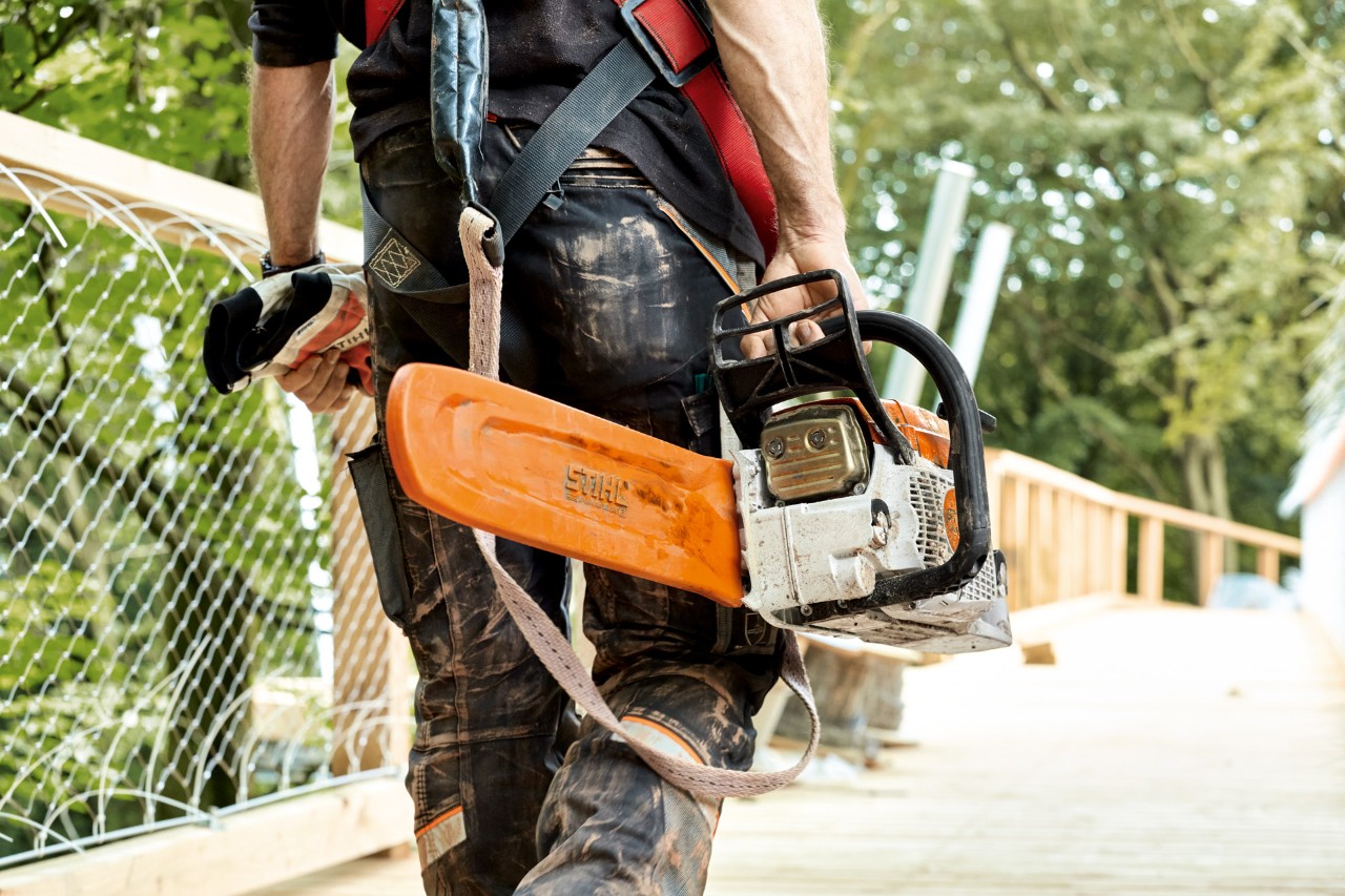 Een man in veiligheidskleding draagt een STIHL benzinekettingzaag MS 261 met kettingbescherming